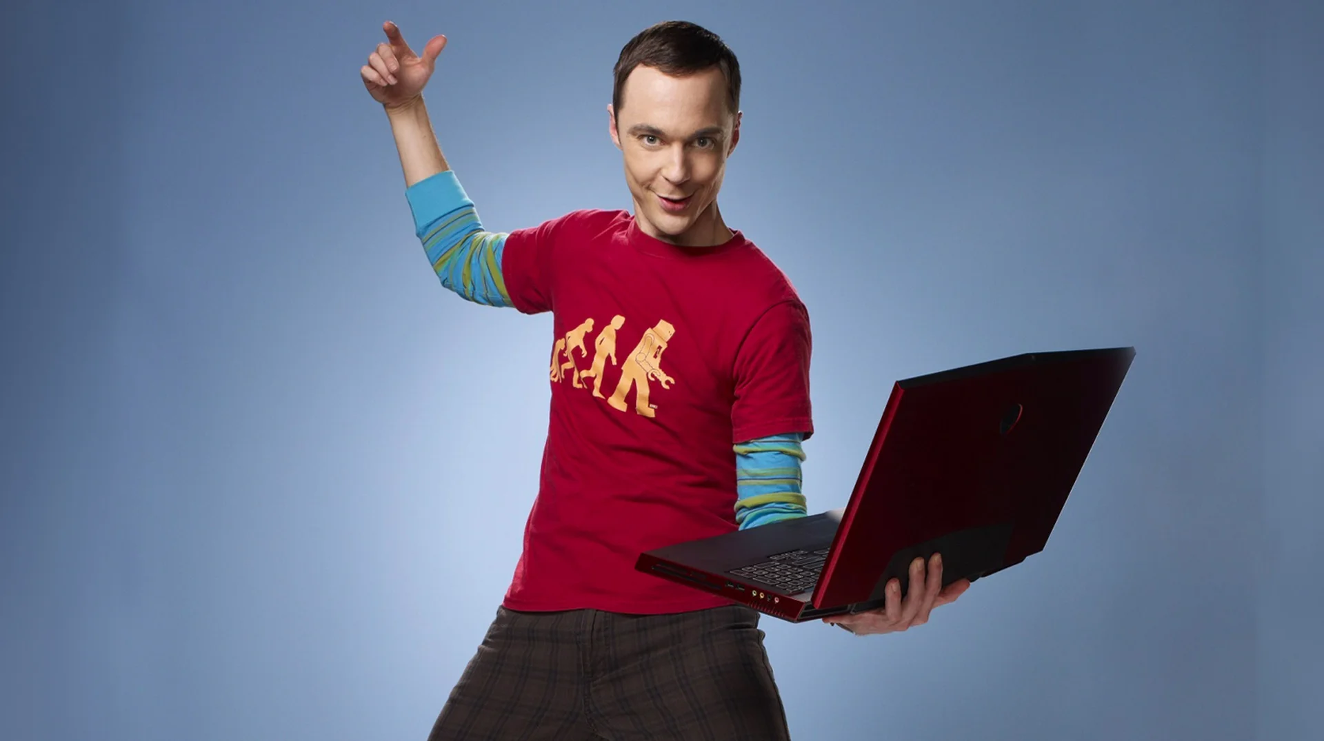 Sheldon Holding a Laptop — Sheldon Cooper posing with one arm raised while holding an open red laptop against a blue backdrop