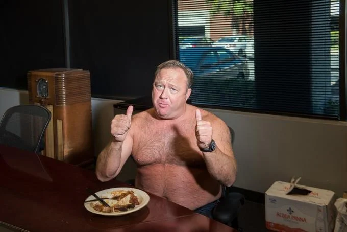 Shirtless Alex Jones at Lunch — Wide shot of shirtless Alex Jones giving two thumbs up at a desk with a plate of food