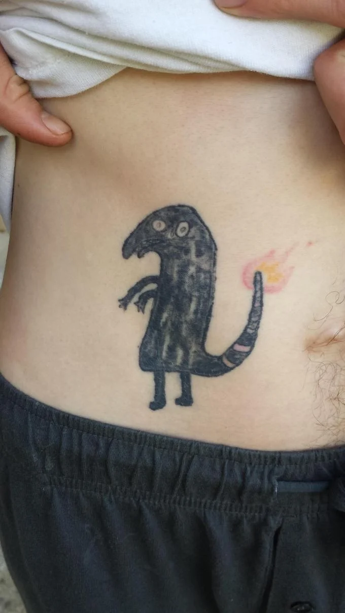 Person revealing a Shitty Charmander tattoo on their lower abdomen