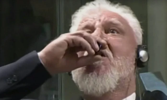 Slobodan Praljak's Courtroom Suicide — Slobodan Praljak in a suit drinking from a small vial in a Hague courtroom.