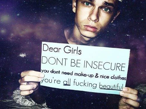 Slut Shaming — A young man holds a handwritten sign about women's insecurity and appearance pressures against a starry background.