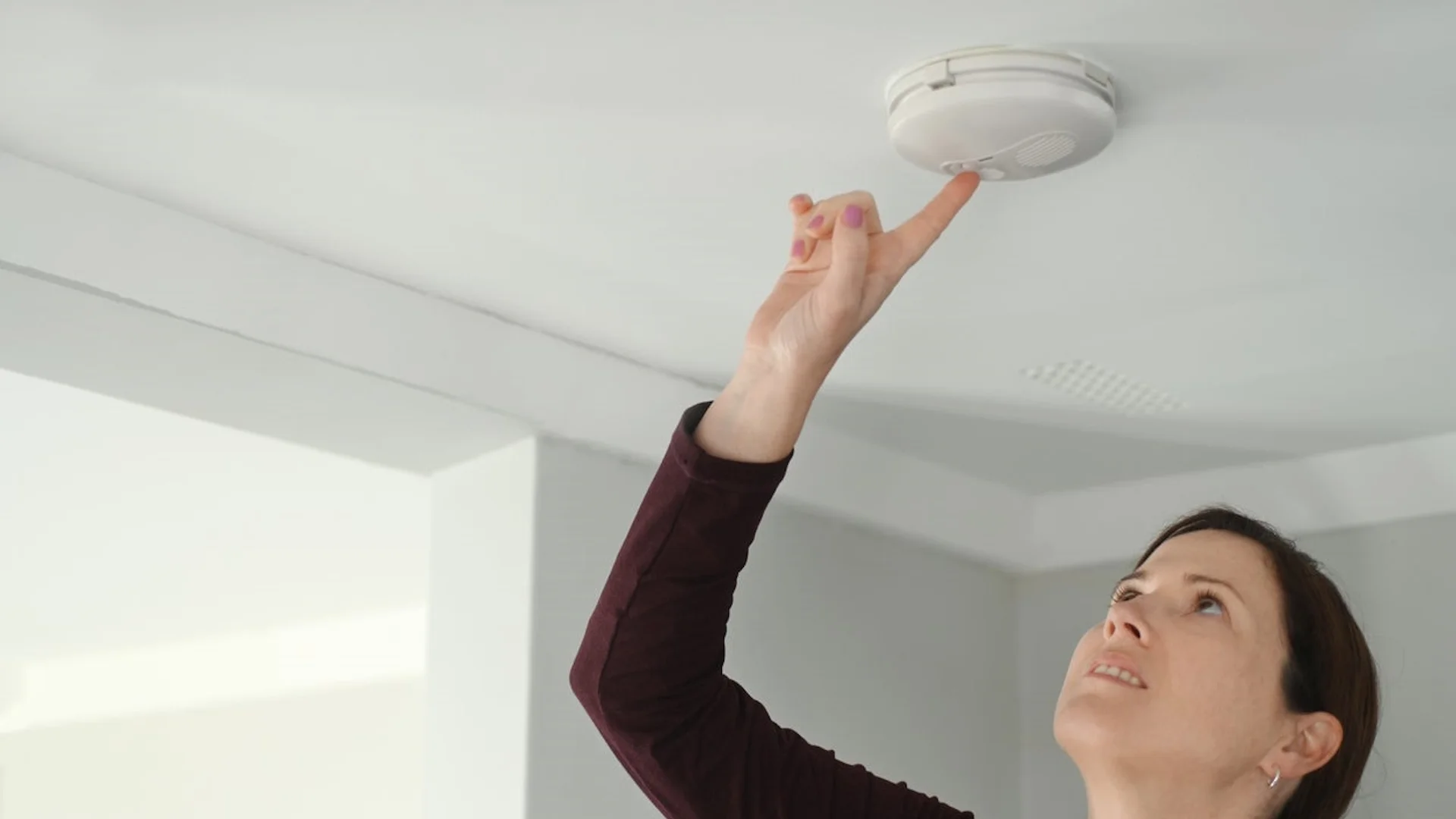 Smoke Detector Beeping — Woman reaching up to press a ceiling-mounted smoke detector