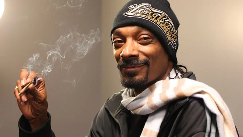 Snoop Dogg in Long Beach beanie smiling and holding a joint with smoke rising