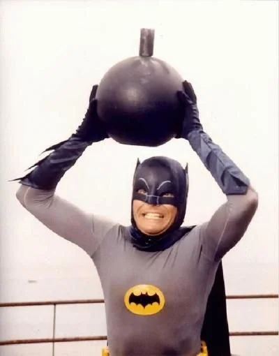 Some Days, You Just Can't Get Rid of a Bomb! — Adam West as Batman holding a round black bomb above his head