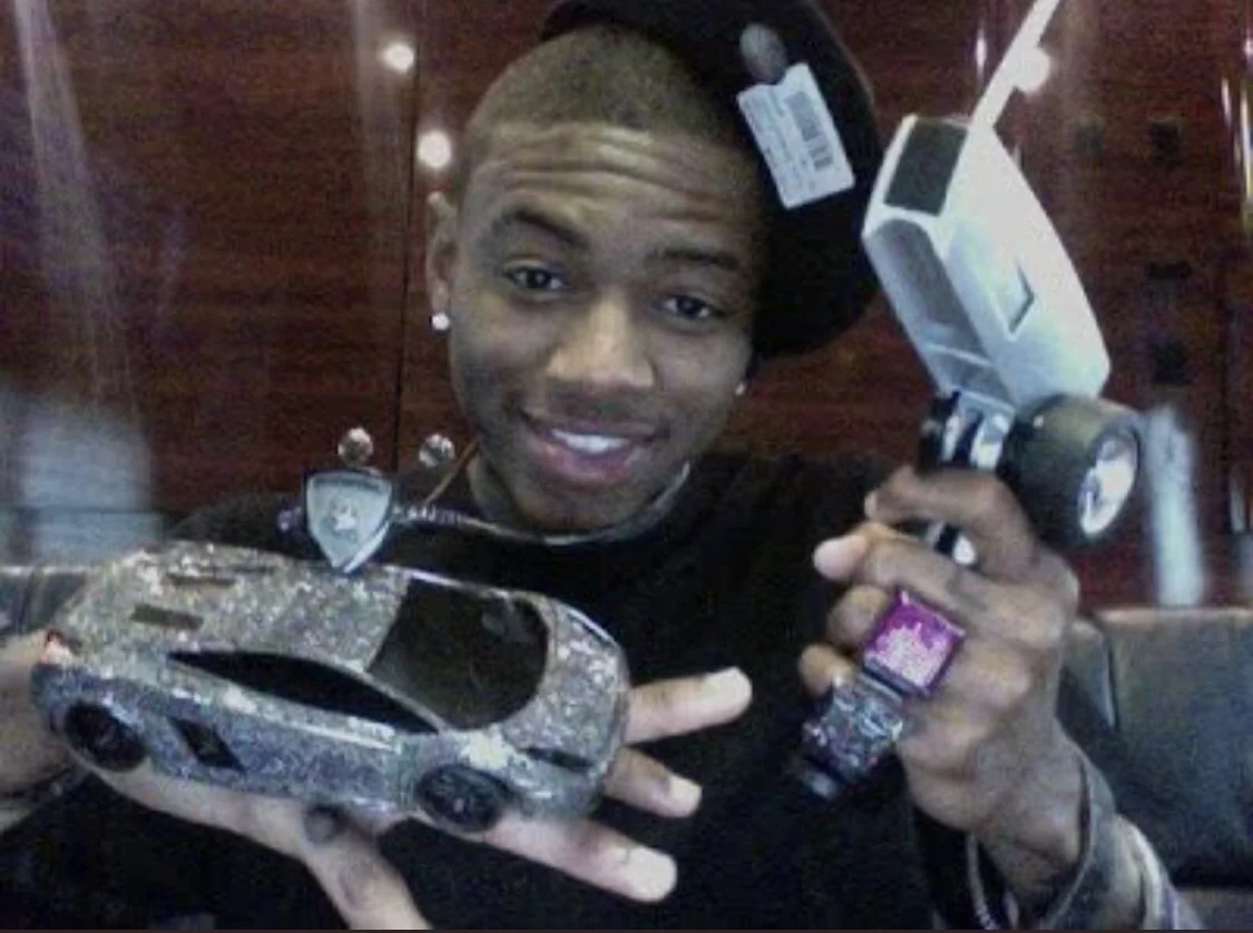 Young Soulja Boy holding a bedazzled toy Lamborghini and jeweled camera