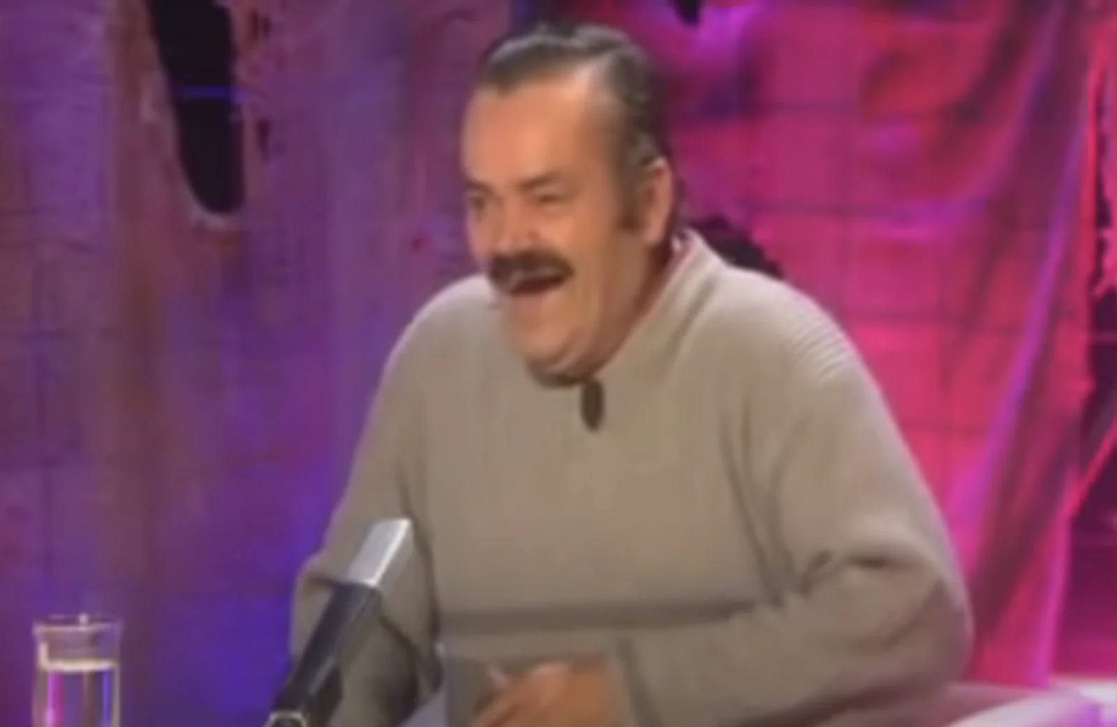 Spanish Laughing Guy — Man with distinctive mustache in midst of infectious laugh wearing light shirt against purple-pink background.