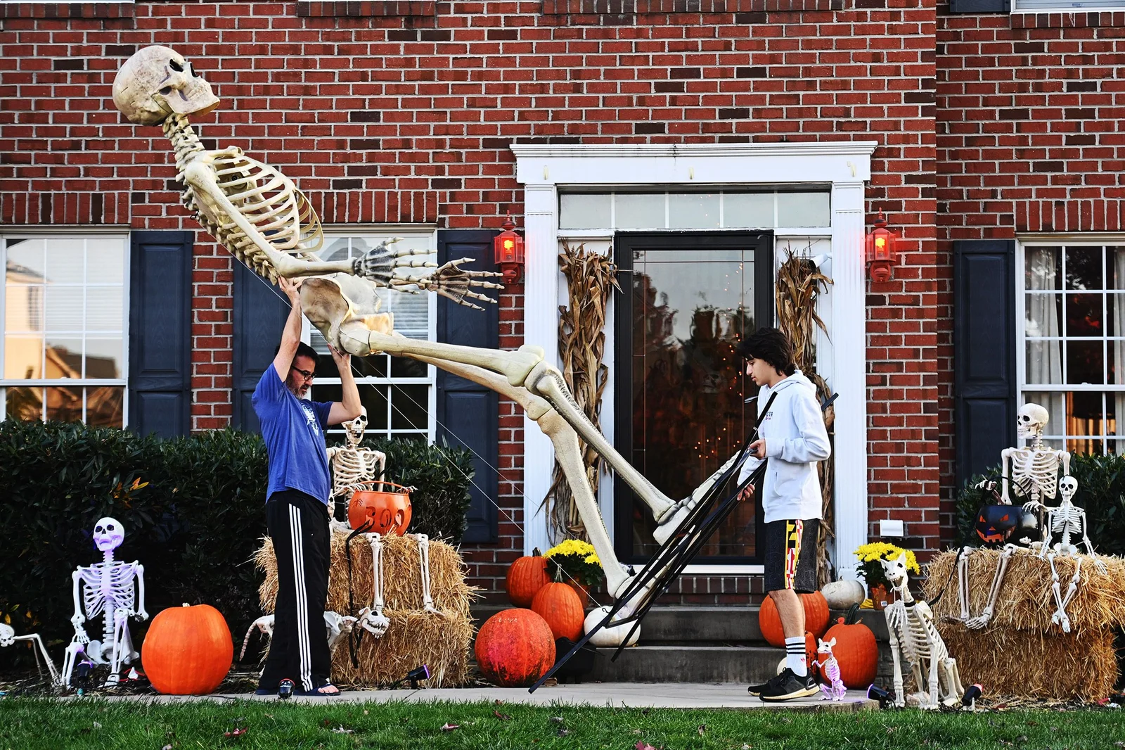 Spooky Scary Skeletons — Two children assembling a large skeleton decoration outside a suburban home surrounded by pumpkins and props.