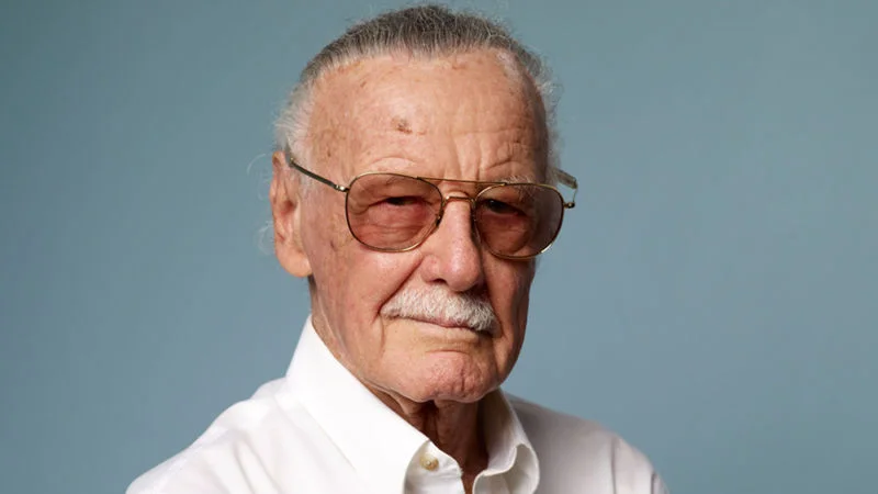 Portrait of Stan Lee wearing tinted aviator glasses and a white collared shirt.