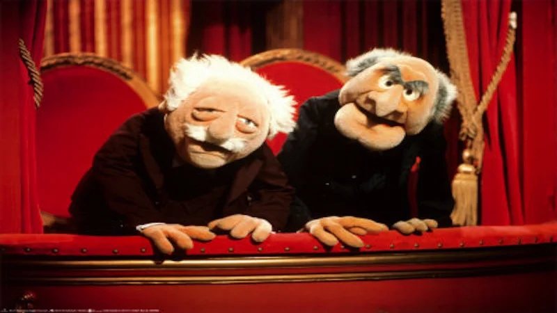 Statler and Waldorf muppets leaning over their red theater balcony