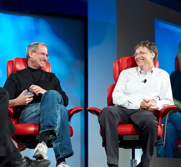 Steve Jobs vs. Bill Gates — Steve Jobs and Bill Gates laughing in red chairs on stage at D5 conference