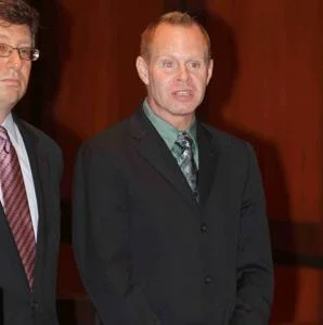 Steven Slater — Photo of middle-aged man in dark suit and green tie at wooden background with another person visible.