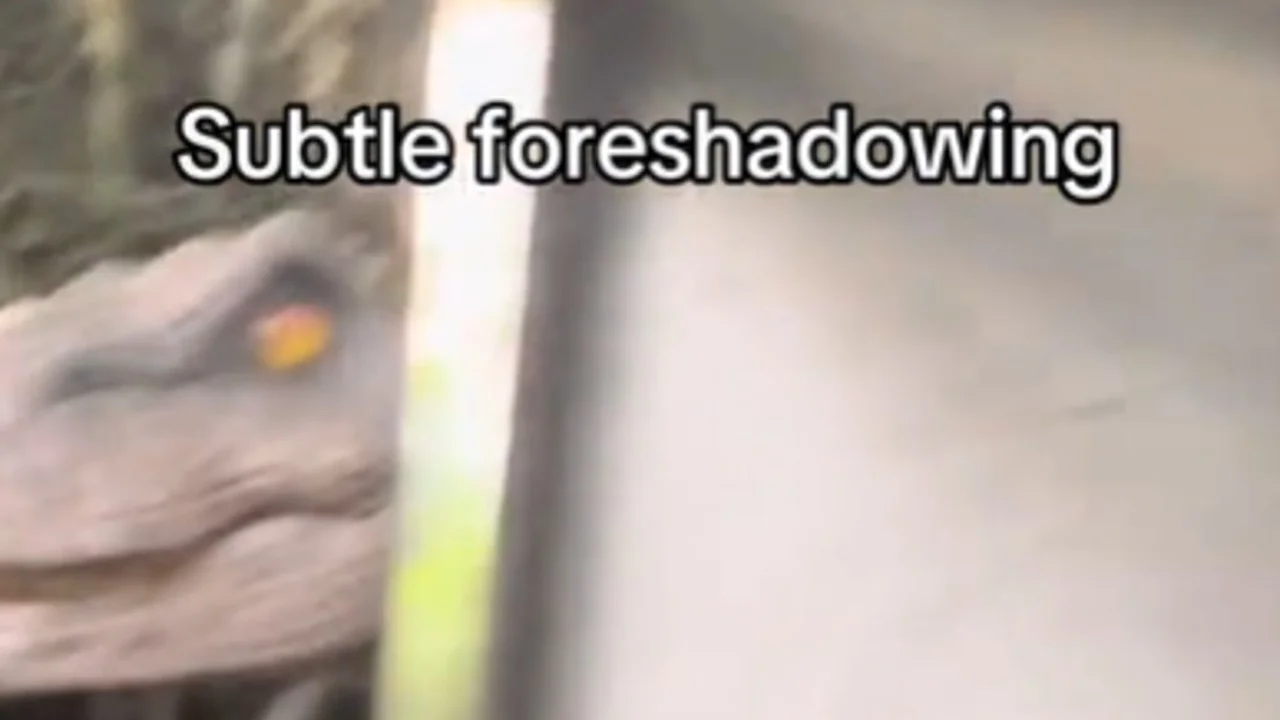 Blurry image of a dinosaur-like creature with a yellow eye peering from behind a pole, with the caption 'Subtle foreshadowing' in bold white text.
