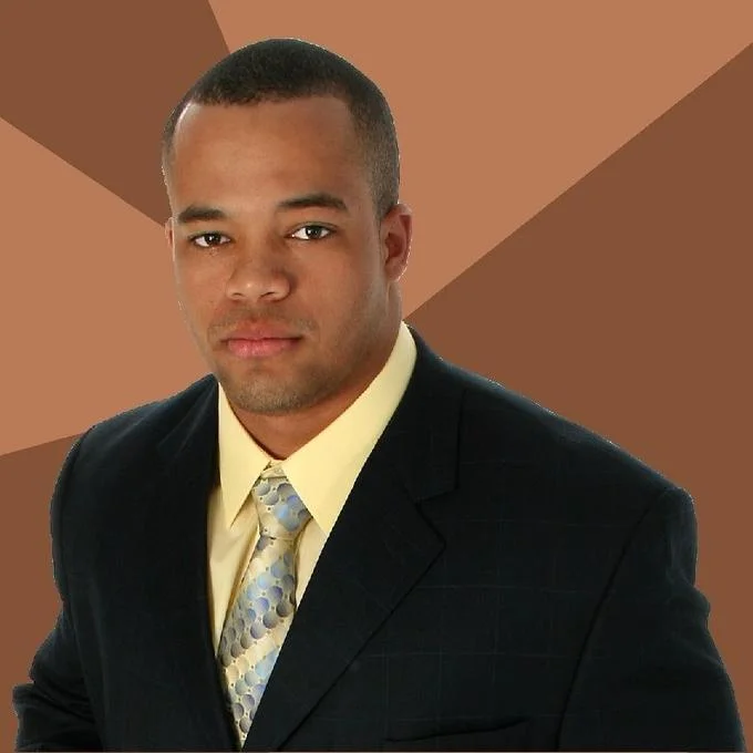 Successful Black Man — Close-up portrait of a Black man in a suit and patterned tie on a brown sunburst background.