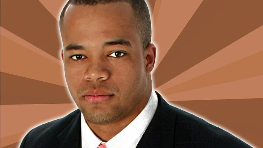 Successful Black Man — Young Black man in a black suit and tie on a brown sunburst background.