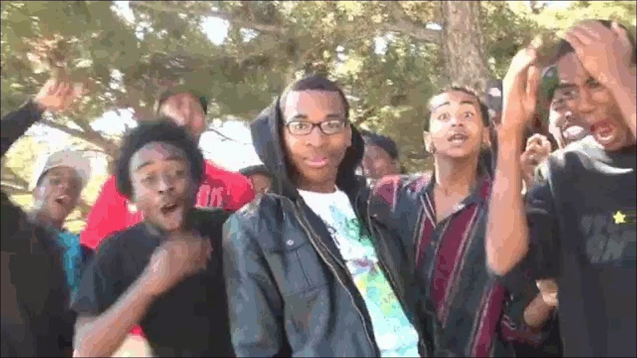 Group of young men reacting with exaggerated excitement outdoors, hands raised and mouths open, from the Supa Hot Fire video.