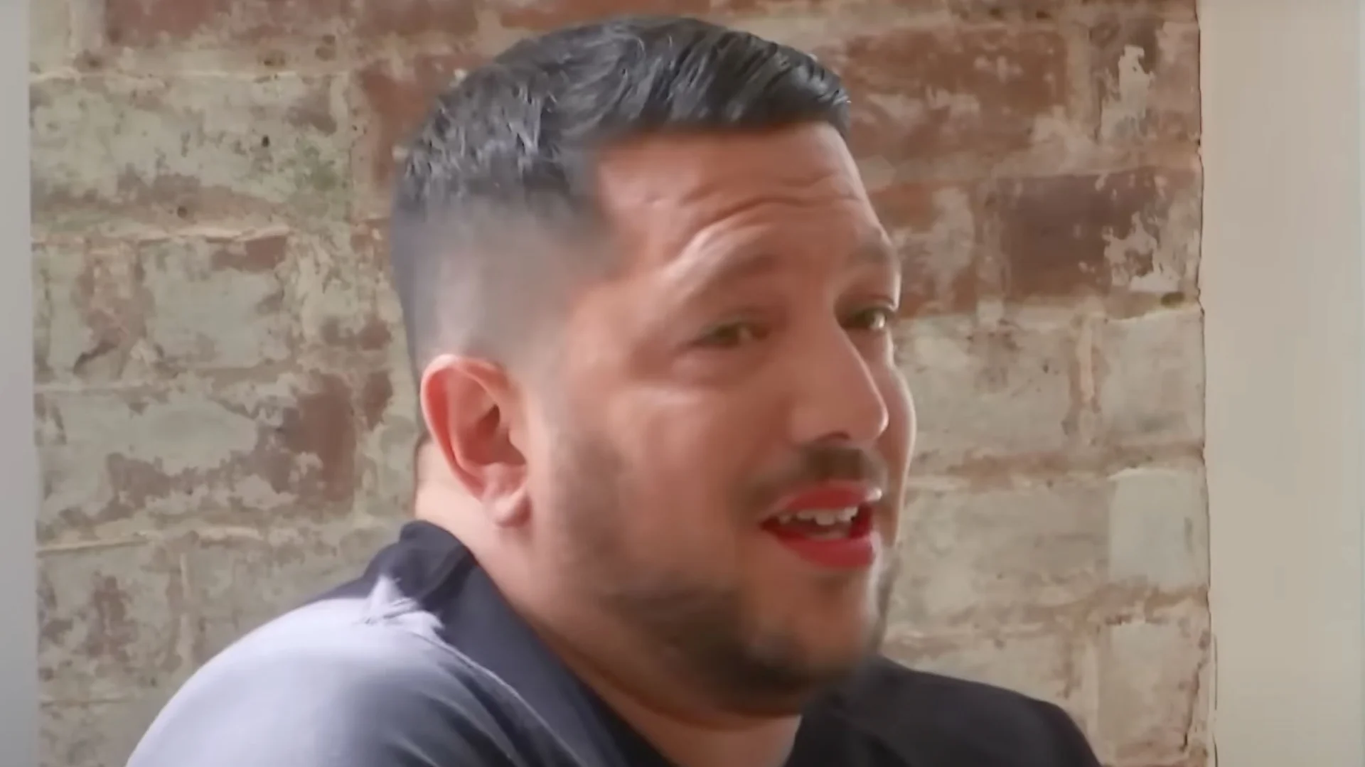 Tanka Jahari — Close-up of man with fade haircut speaking in front of brick wall