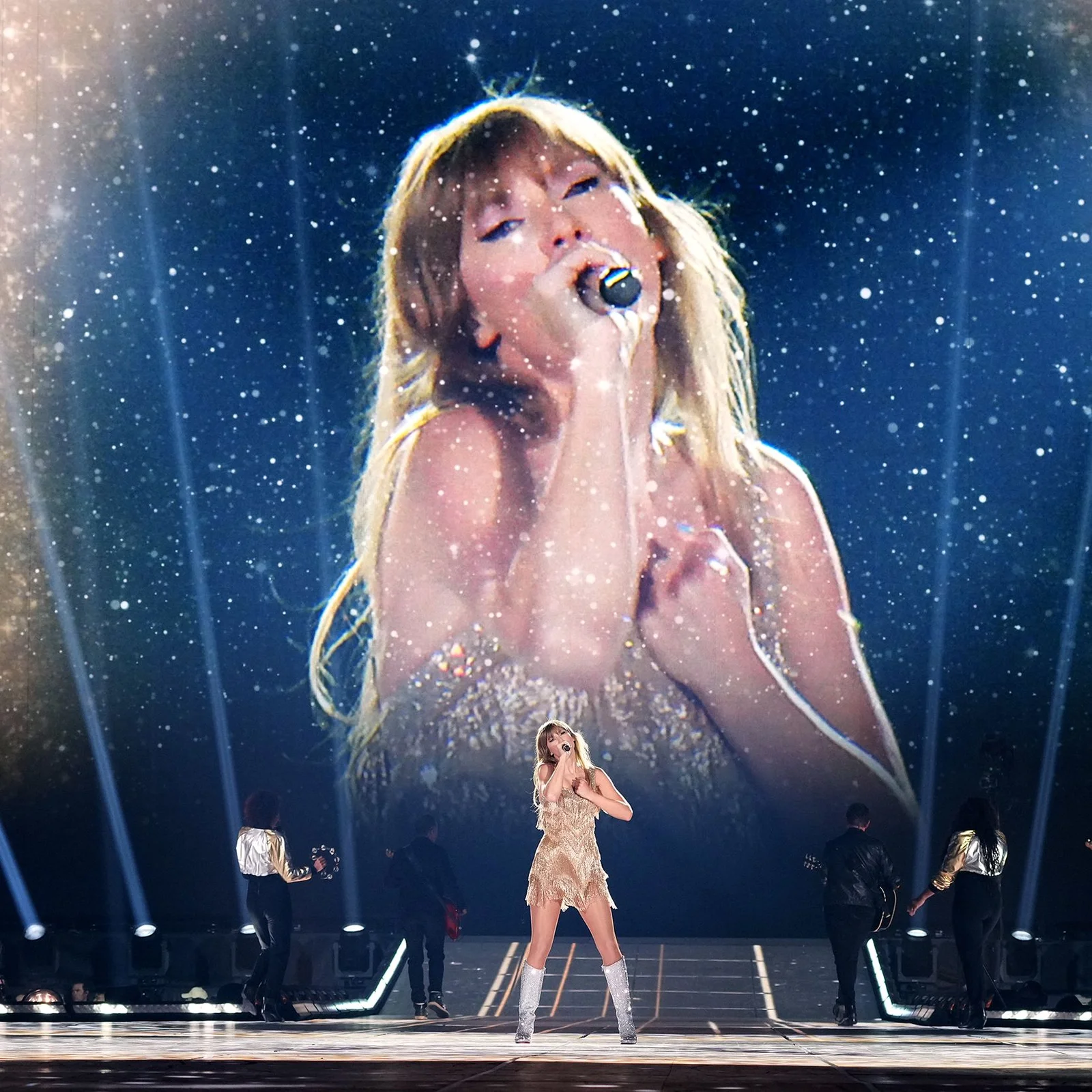 Taylor Swift Eras Tour — Wide-angle stage photo with Taylor Swift and backup dancers under blue spotlights.