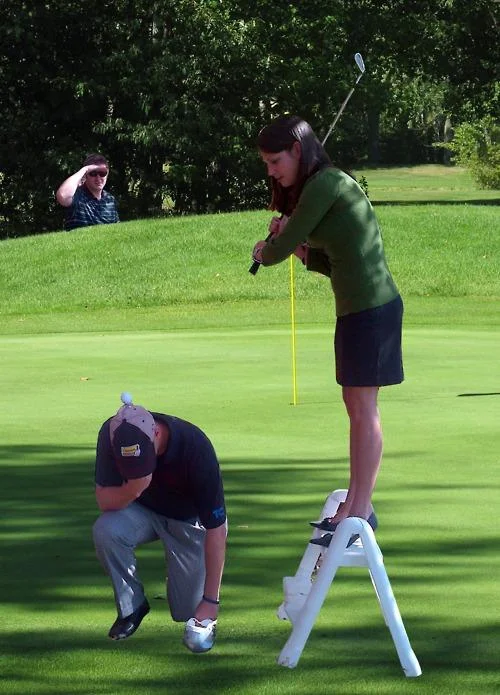 Golfer performing Tebowing while balanced on ladder held by another person.