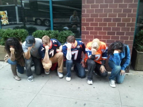 Row of people in sports jerseys performing Tebowing pose in unison.