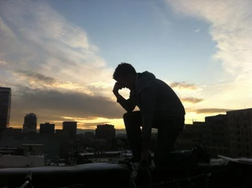 Silhouetted figure performing Tebowing pose on rooftop against dramatic sunset sky.