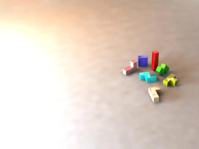 Small colorful 3D Tetris pieces scattered on a bright neutral surface