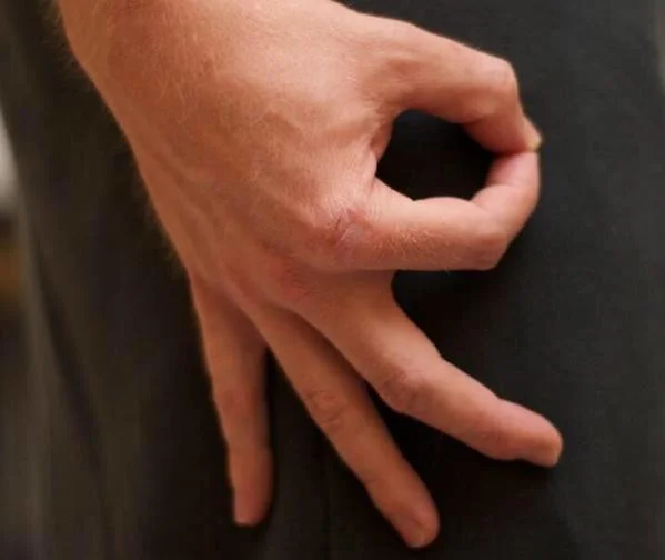 The Circle Game — Hand making the OK circle gesture against dark pants