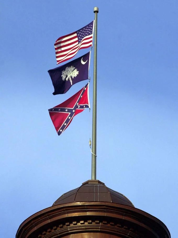 The Confederate Flag Debate — Flagpole flying U.S. flag, South Carolina flag, and Confederate battle flag above a state capitol dome