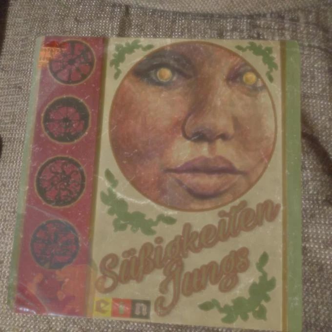 The Most Mysterious Song On The Internet — A photograph of a vinyl record sleeve featuring stylized artwork of a face with golden eyes and botanical motifs.