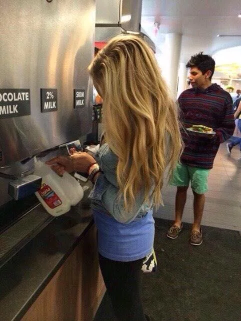 The Struggle Is Real — Woman with very long blonde hair filling milk jug at a cafeteria dispenser