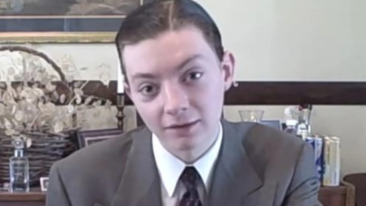 TheReportOfTheWeek YouTuber John Jurasek in suit and tie seated at desk