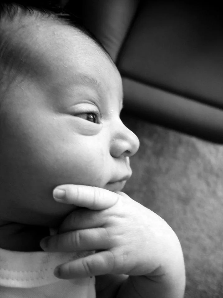 Thinking Baby — Black-and-white close-up of a newborn baby resting chin on hand in a thoughtful pose