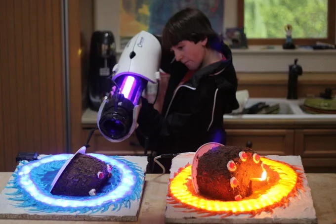 Thinking With Portals — Child with Portal gun prop and two cakes decorated with glowing orange and blue portal rings