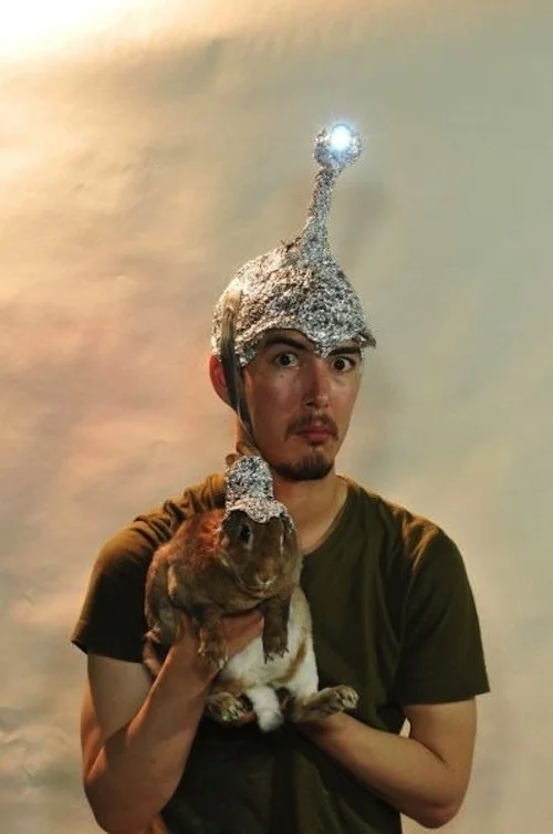 Tin Foil Hats — Man in LED-topped tin foil helmet holding a rabbit wearing a miniature tin foil hat.