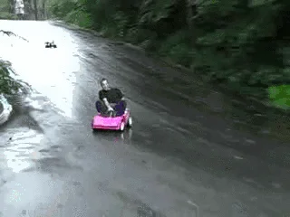 Tokyo Drift In A Barbie Car — Wide aerial view of driveway scene with toy and surrounding landscape.