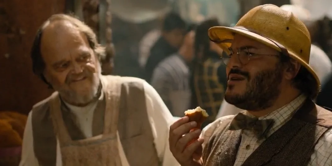 Too Many Cooks — Two men at a party, one with a safari helmet holding food, the other smiling beside him.