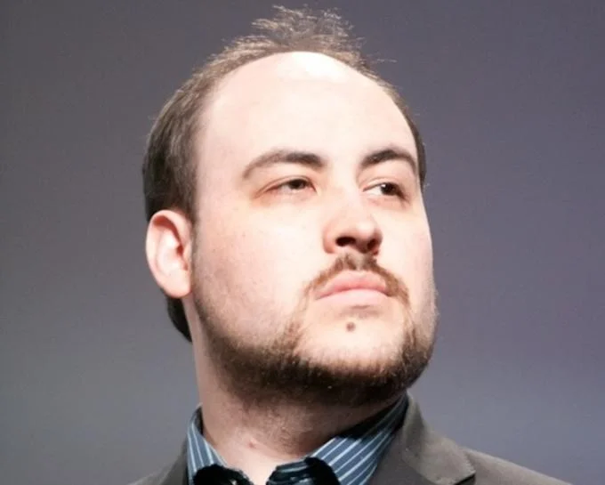 Portrait photo of John TotalBiscuit Bain wearing a suit