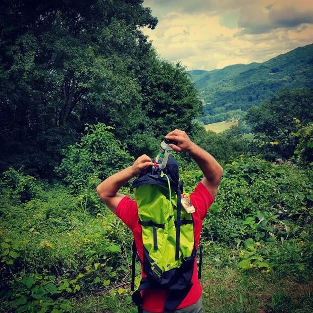 Trashtag — Hiker in red shirt with green backpack overlooking a green mountain valley.