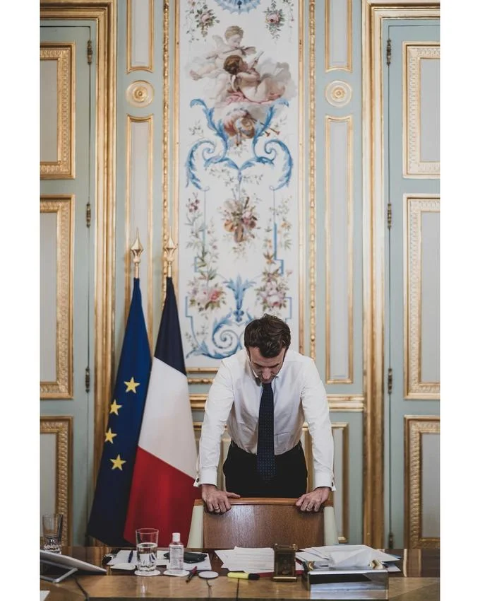 Troubled Macron — Macron leans on a chair with head bowed in a gilded Élysée office with French and EU flags