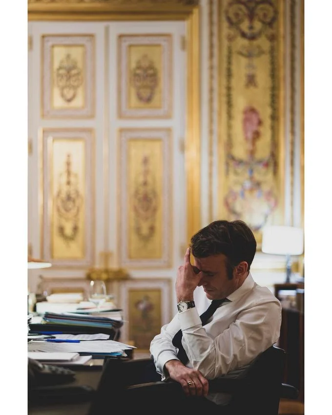 Troubled Macron — Macron sits at desk pinching his nose with hand against forehead in gilded office