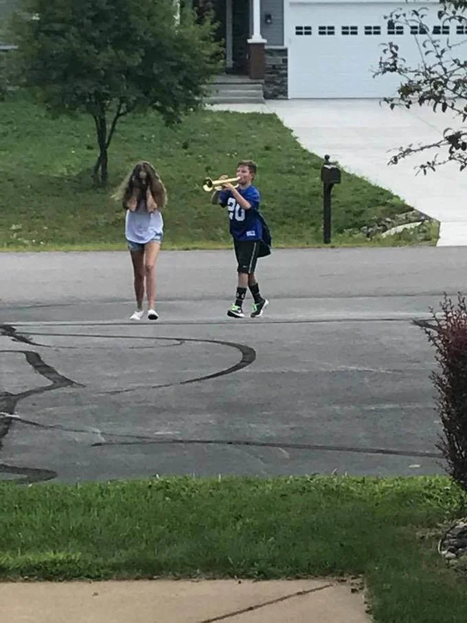 Trumpet Boy — Uncropped source photo of boy playing trumpet at girl covering her face in suburban driveway