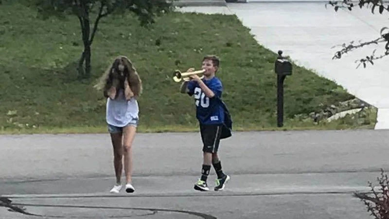 Trumpet Boy — Boy in blue jersey playing trumpet at a distressed girl covering her face on a driveway