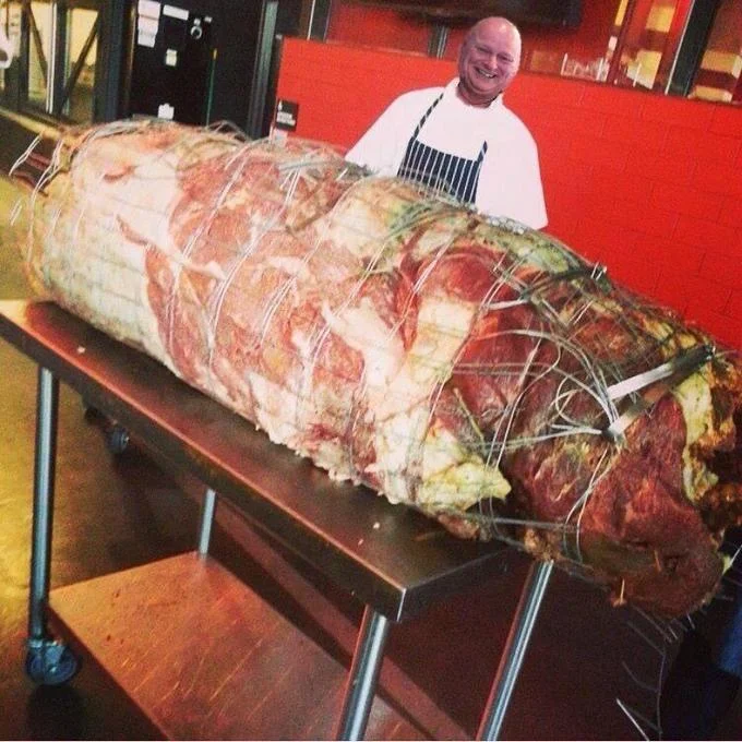 Turducken — Chef posing behind a giant trussed meat roast on a kitchen cart.