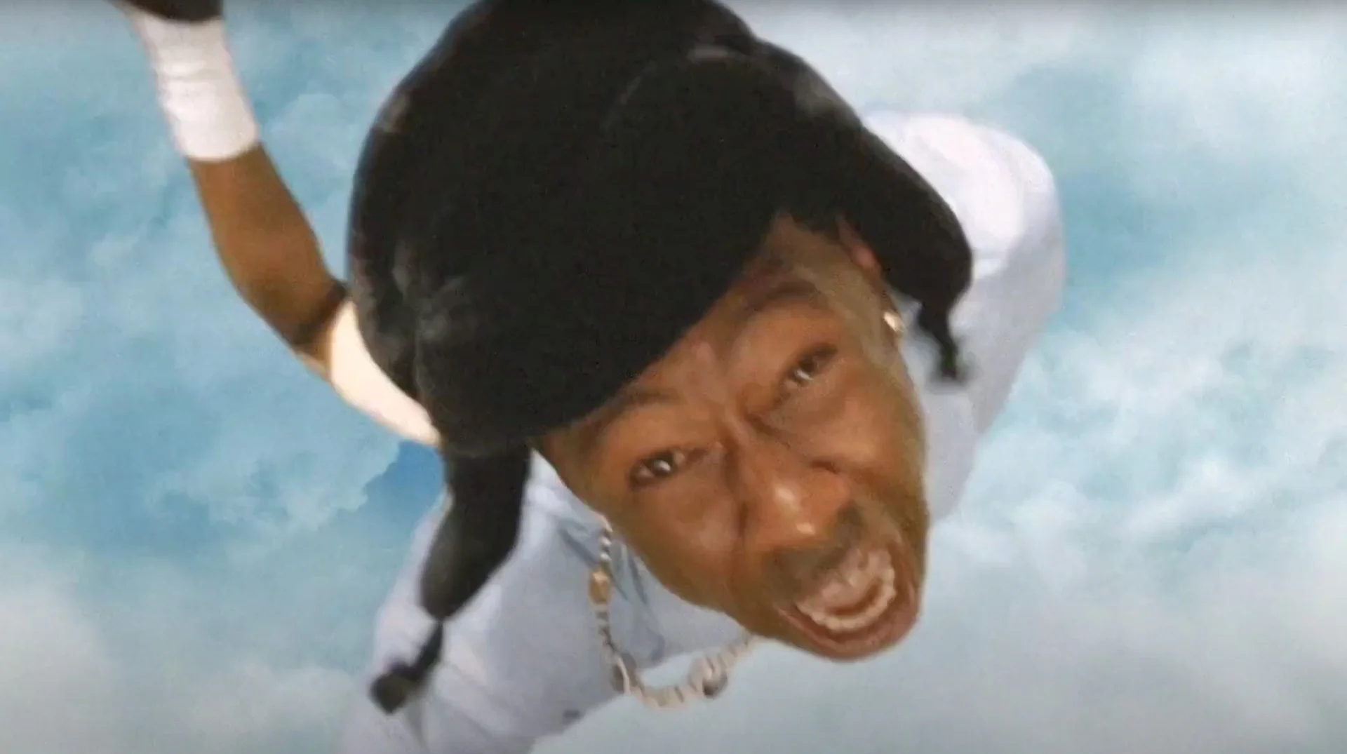 Tyler, The Creator Falling From The Sky — Tyler, the Creator falling through the sky with arm raised and face contorted, viewed from below against cloudy