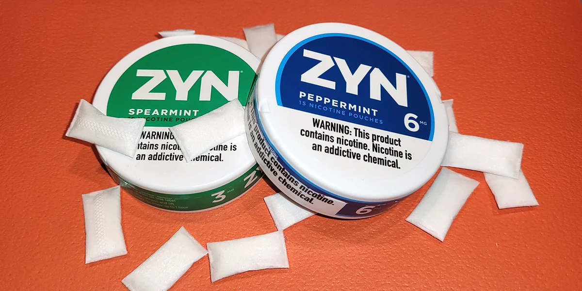 Upper Decky Zynnies, Upper Decky Lip Pillows, Ferda — Two ZYN nicotine pouch cans in Spearmint and Peppermint flavors with loose white pouches scattered on an