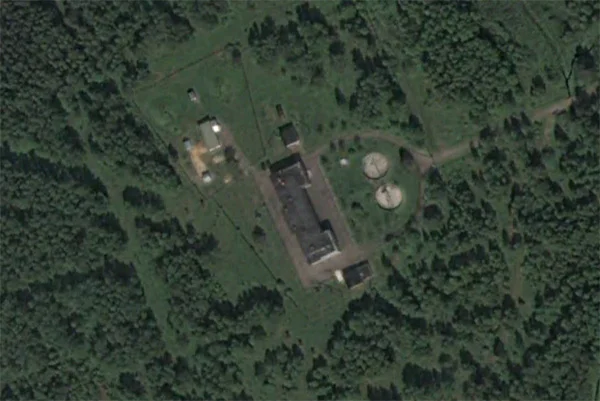 UVB-76 Mystery — Aerial satellite view of the UVB-76 compound with main building, outbuildings, and tanks in a forest clearing