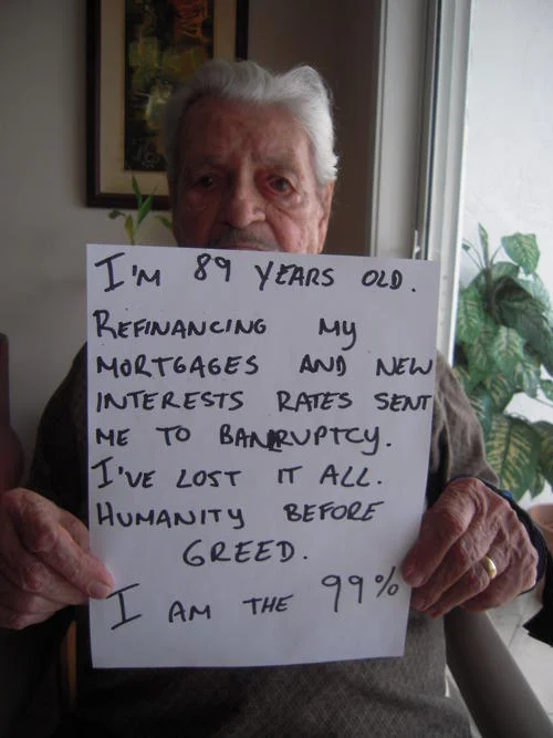 We Are The 99 Percent — Elderly man holds a handwritten sign about mortgage refinancing bankruptcy, declaring 'I am the 99%'.