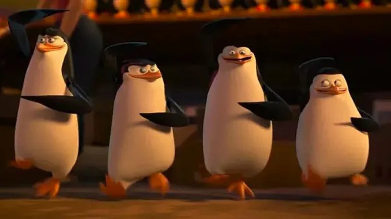 Well Boys, We Did It. Racism Is No More — Four Madagascar penguins walking in formation inside a dimly lit setting