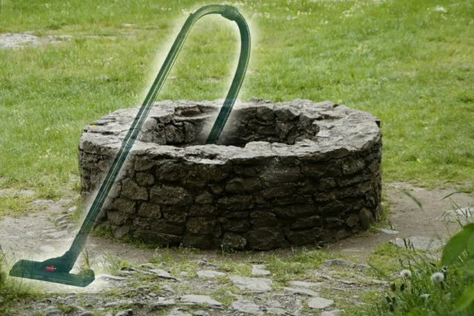 Well That Sucks — Stone wishing well with green vacuum cleaner hose arched over it