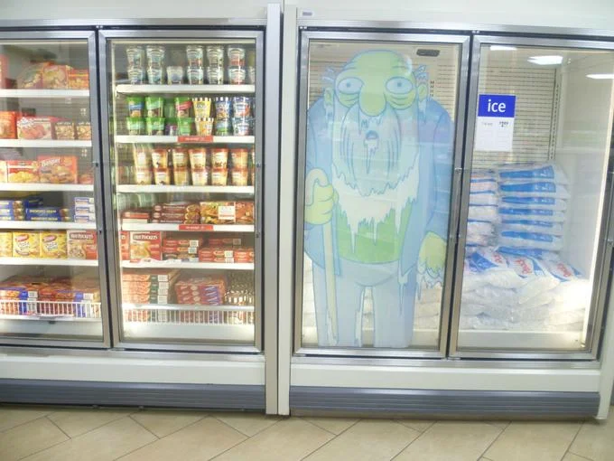 What a Time to Be Alive — Grocery store freezer doors with a cartoon illustration of an elderly bearded man beside shelves of frozen food and bagged ice