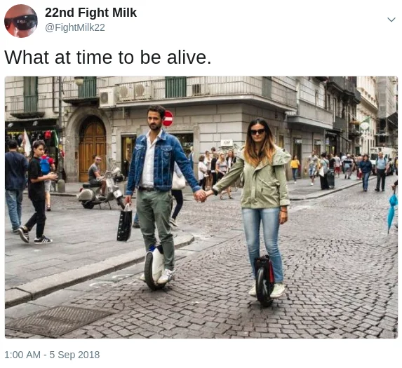 What a Time to Be Alive — Tweet showing a couple holding hands while riding electric unicycles down a cobblestone street, captioned 'What at time to be alive'